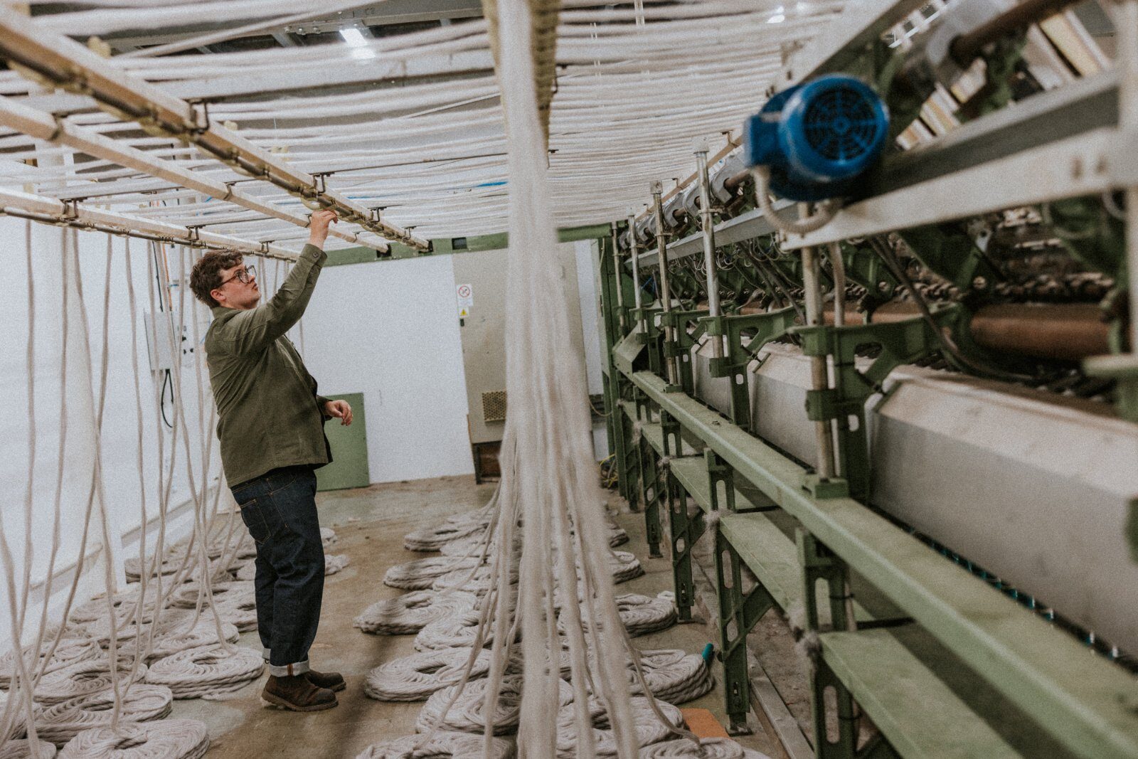 A member of the team checking hanging roving above the machinery, with coiled fibre laid out below