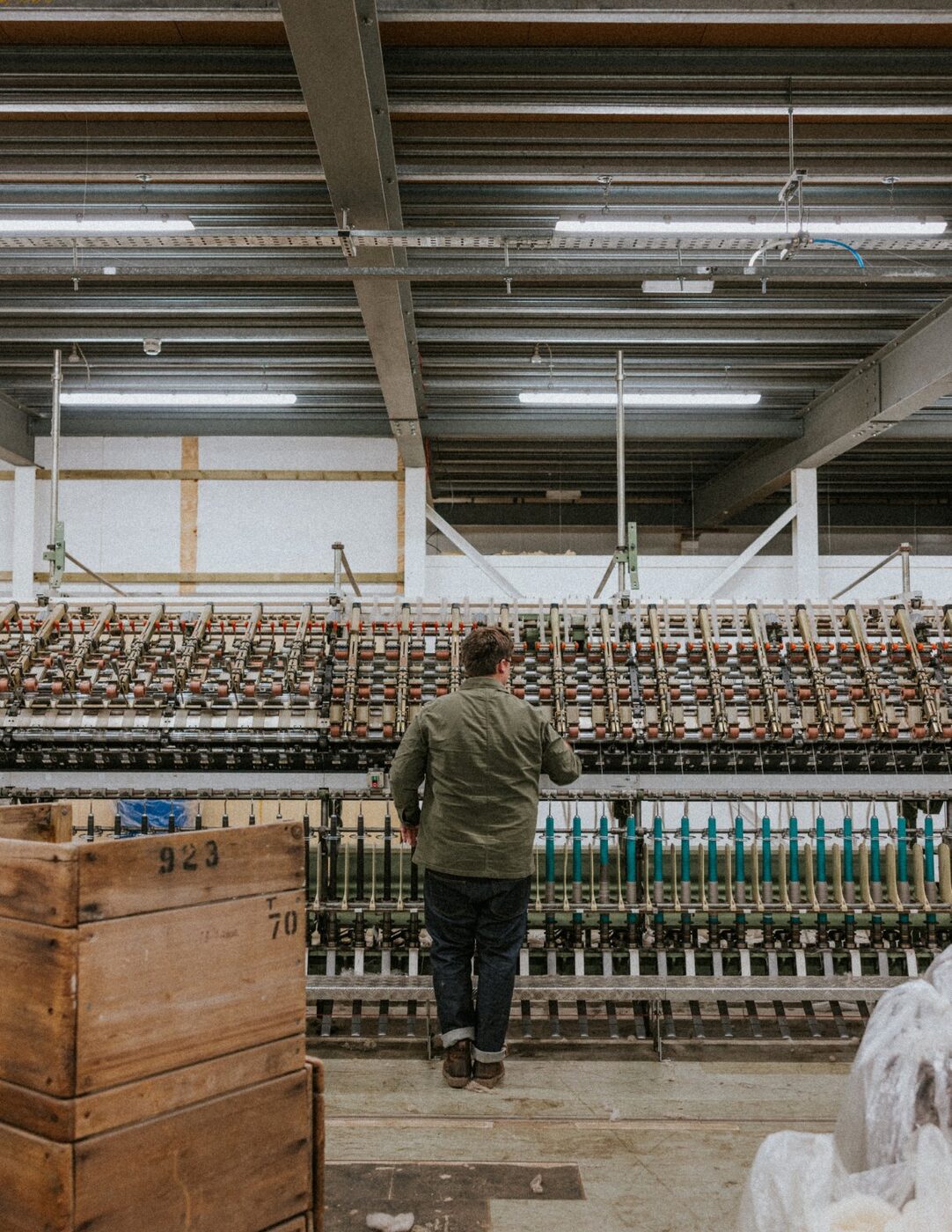 A member of the team working at a spinning frame inside the mill, wooden crate in the foreground