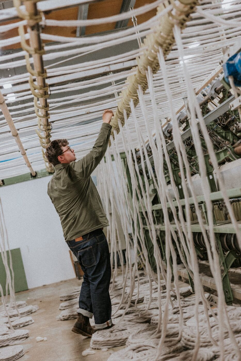 A member of the team reaching up to check hanging roving above the spinning machinery